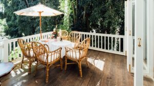 Hardhouten terras met rotan stoelen, ronde tafel en parasol, omringd door weelderig groen