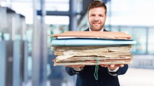 Man in pak houdt een stapel papieren dossiers vast, illustratief voor tastbare communicatie met papier