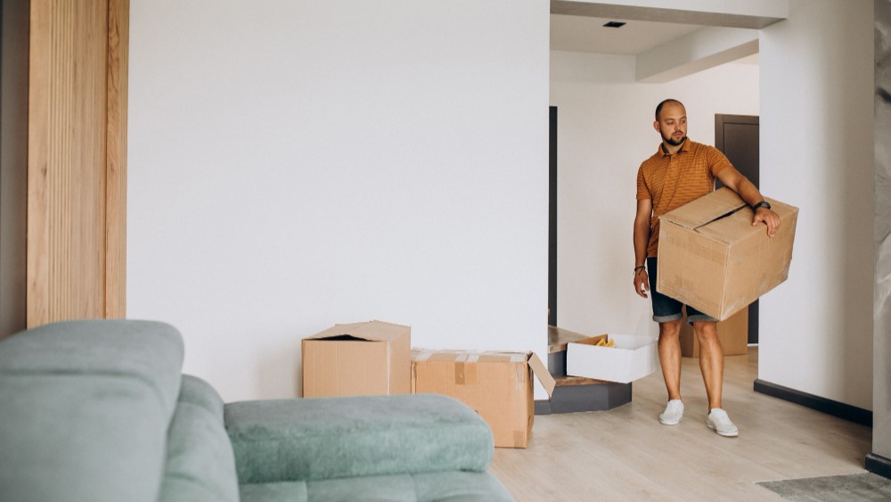 Man draagt verhuisdoos in woonkamer tijdens het efficiënt verhuizen van zijn inboedel