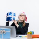 Vrouw met kerstoutfit toont trots een ingepakt cadeau tijdens een duurzame kerst op kantoor.