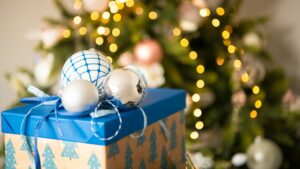 Cadeau met blauwe kerstversiering voor een luxe decembercadeau, geplaatst voor een verlichte kerstboom.