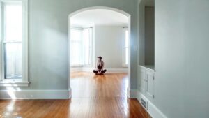 Vrouw zit op houten vloer in lichte, lege kamer als onderdeel van een huis verkopen checklist