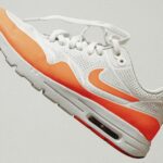 Witte sneaker met oranje details zwevend tegen een neutrale achtergrond, geschikt voor tips over schoenen wassen