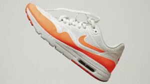 Witte sneaker met oranje details zwevend tegen een neutrale achtergrond, geschikt voor tips over schoenen wassen
