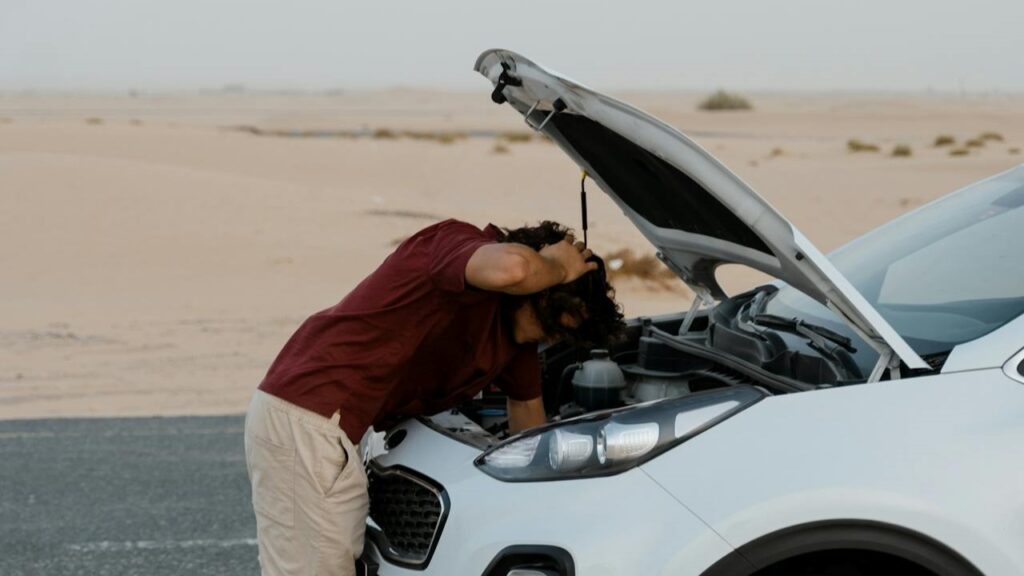 Man onderzoekt met zorg de motor van een stilgevallen auto – autoproblemen voorkomen begint met alertheid.