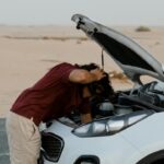 Man onderzoekt met zorg de motor van een stilgevallen auto – autoproblemen voorkomen begint met alertheid.