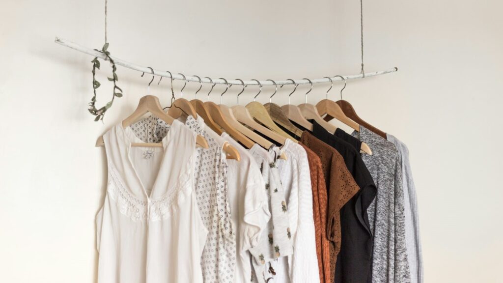 Kledingstukken in zachte kleuren en strakke lijnen hangen op houten hangers aan een minimalistische kledingstang