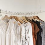 Kledingstukken in zachte kleuren en strakke lijnen hangen op houten hangers aan een minimalistische kledingstang