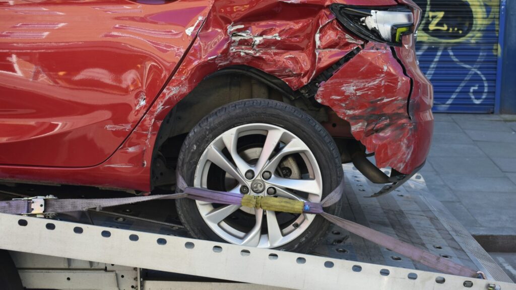 Achterzijde van een zwaar beschadigde rode auto op een sleepwagen na een ongeluk, een van de eerste stappen na een ongeluk.