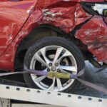 Achterzijde van een zwaar beschadigde rode auto op een sleepwagen na een ongeluk, een van de eerste stappen na een ongeluk.