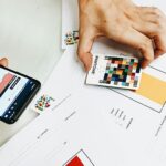Persoon vergelijkt kleurstalen met digitale data op smartphone voor nauwkeurig kleurgebruik op website