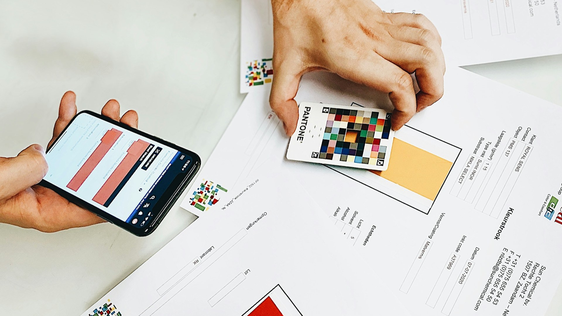 Persoon vergelijkt kleurstalen met digitale data op smartphone voor nauwkeurig kleurgebruik op website