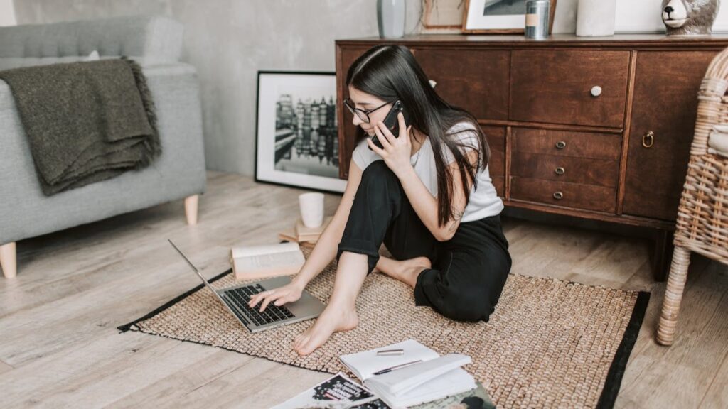 Vrouw die vanuit huis werkt en prioriteiten stelt met laptop, notitieboek en telefoon op de vloer