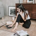 Vrouw die vanuit huis werkt en prioriteiten stelt met laptop, notitieboek en telefoon op de vloer